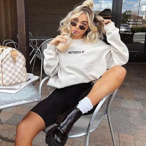 Woman in casual outfit drinking iced coffee at an outdoor cafe.